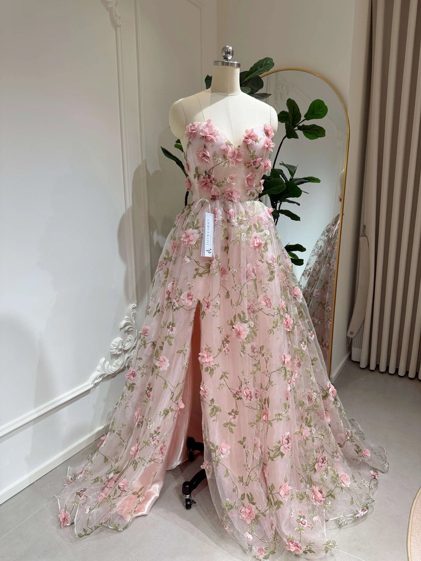Pink 3D floral organza prom gown with green leaf embroidery, sweetheart neckline, and a high side slit on a mannequin.
