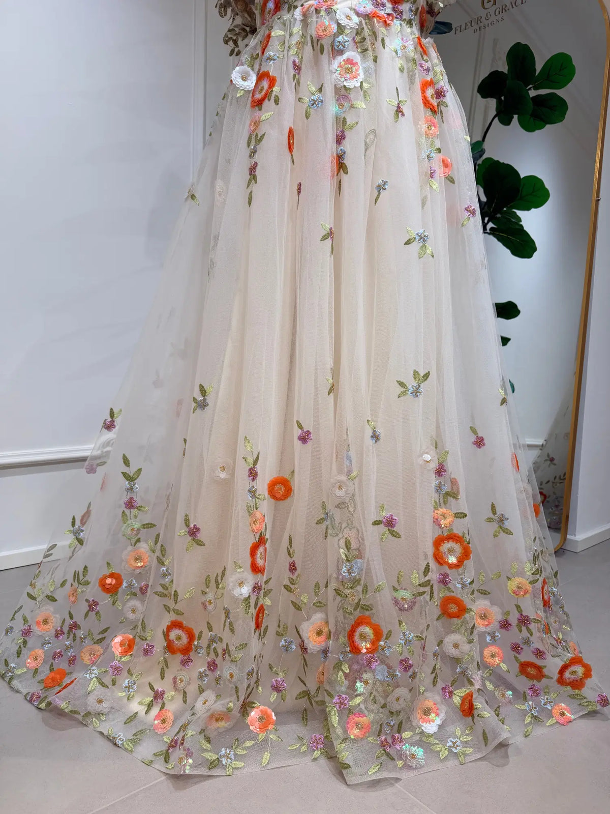 Whimsical A-line wedding dress in sheer tulle with vibrant multicolor floral embroidery and a flowing, garden-inspired skirt.