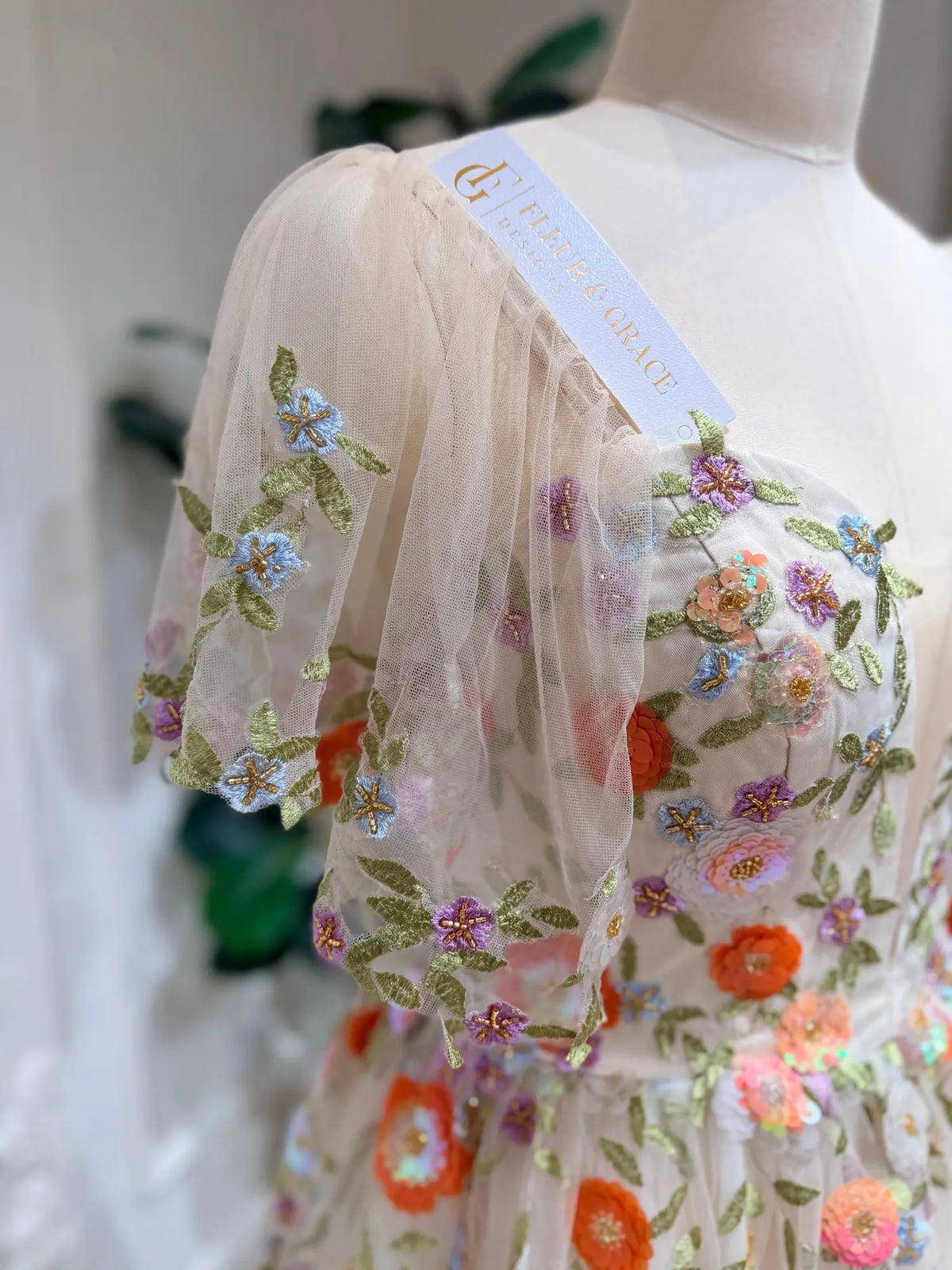 Raya wedding dress with sheer tulle, colorful floral embroidery, and romantic angel sleeves on a mannequin.