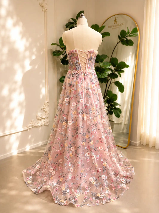 Blush pink tulle prom dress featuring intricate floral embroidery, a structured corset bodice, and a romantic lace-up back.