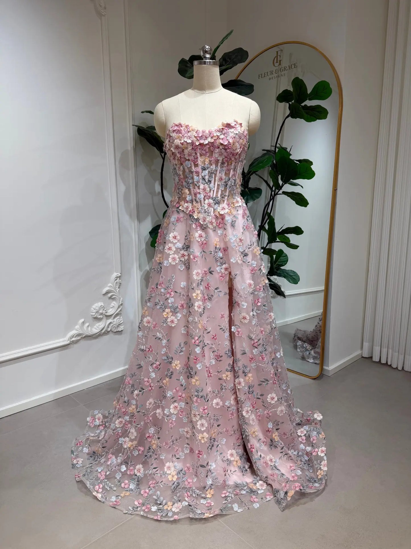 Blush pink tulle prom dress featuring a floral embroidered corset bodice, A-line skirt, and a dramatic high side slit.