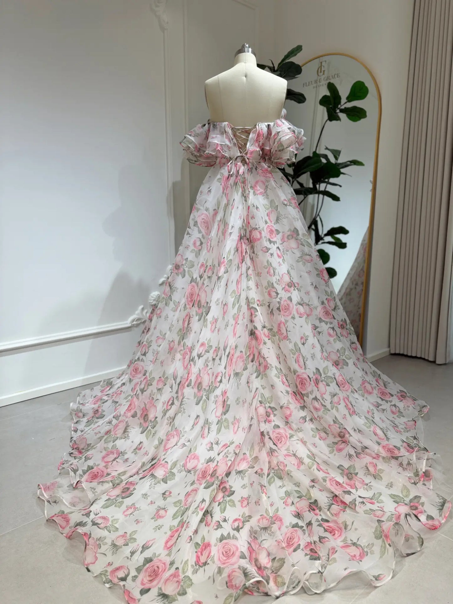 off‑the‑shoulder pink floral printed organza dress with tiered ruffle neckline, functional pockets, and flowing A‑line skirt, ideal for wedding photography and fairy‑tale events.-Model wearing the Rosie Gown FG026 by Fleur&Grace Designs 