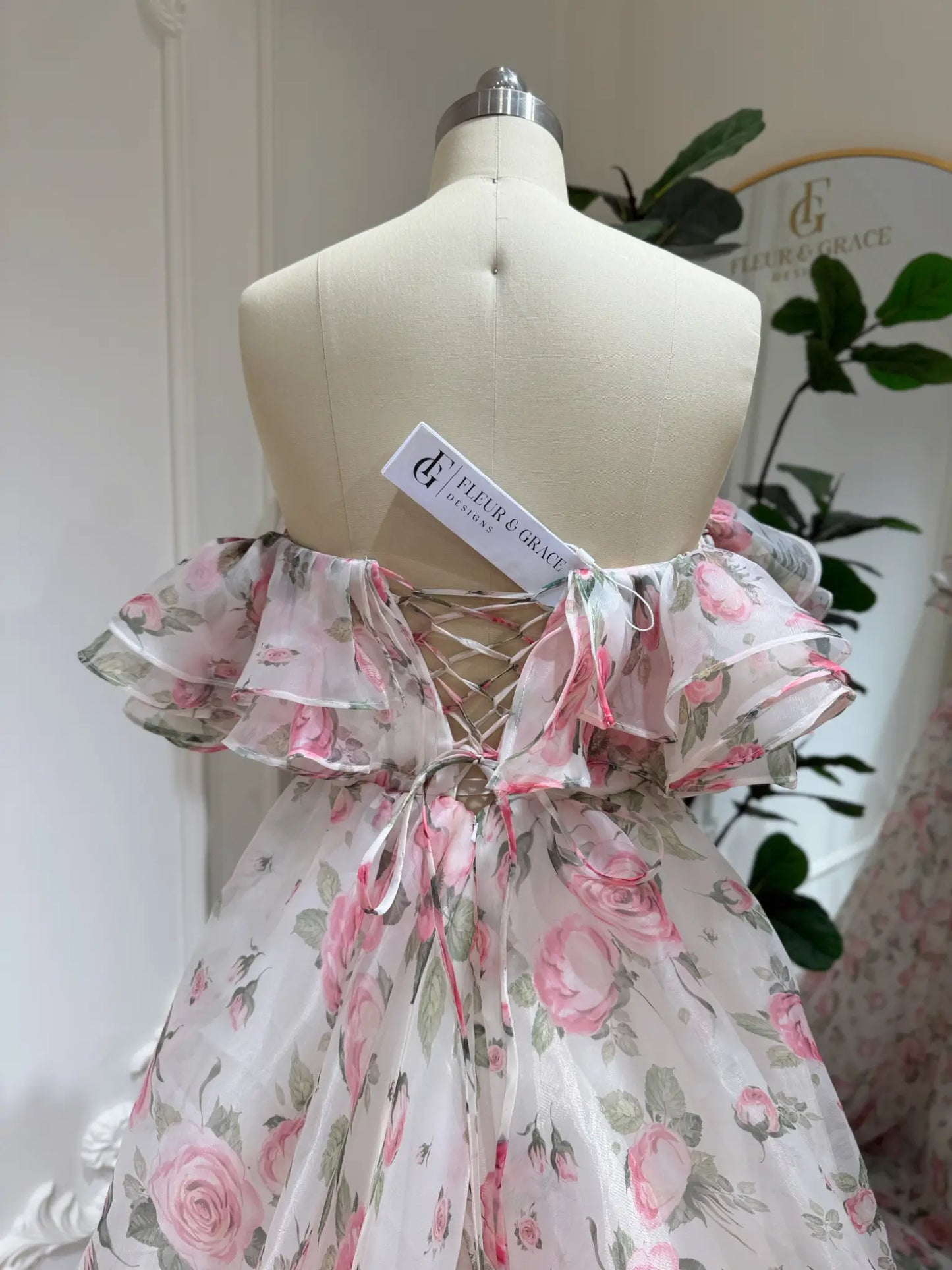 off‑the‑shoulder pink floral printed organza dress with tiered ruffle neckline, functional pockets, and flowing A‑line skirt, ideal for wedding photography and fairy‑tale events.-Model wearing the Rosie Gown FG026 by Fleur&Grace Designs 