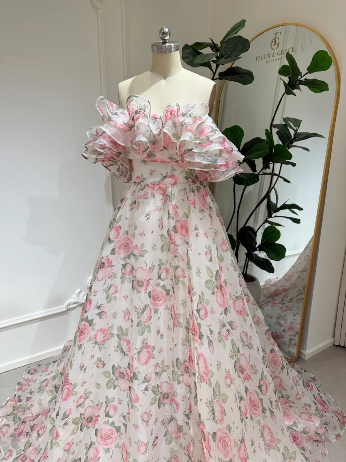 Pink floral organza A-line gown with a tiered ruffle off-the-shoulder neckline on a dress form.