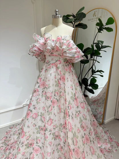 Pink floral organza A-line gown with a tiered ruffle off-the-shoulder neckline on a dress form.