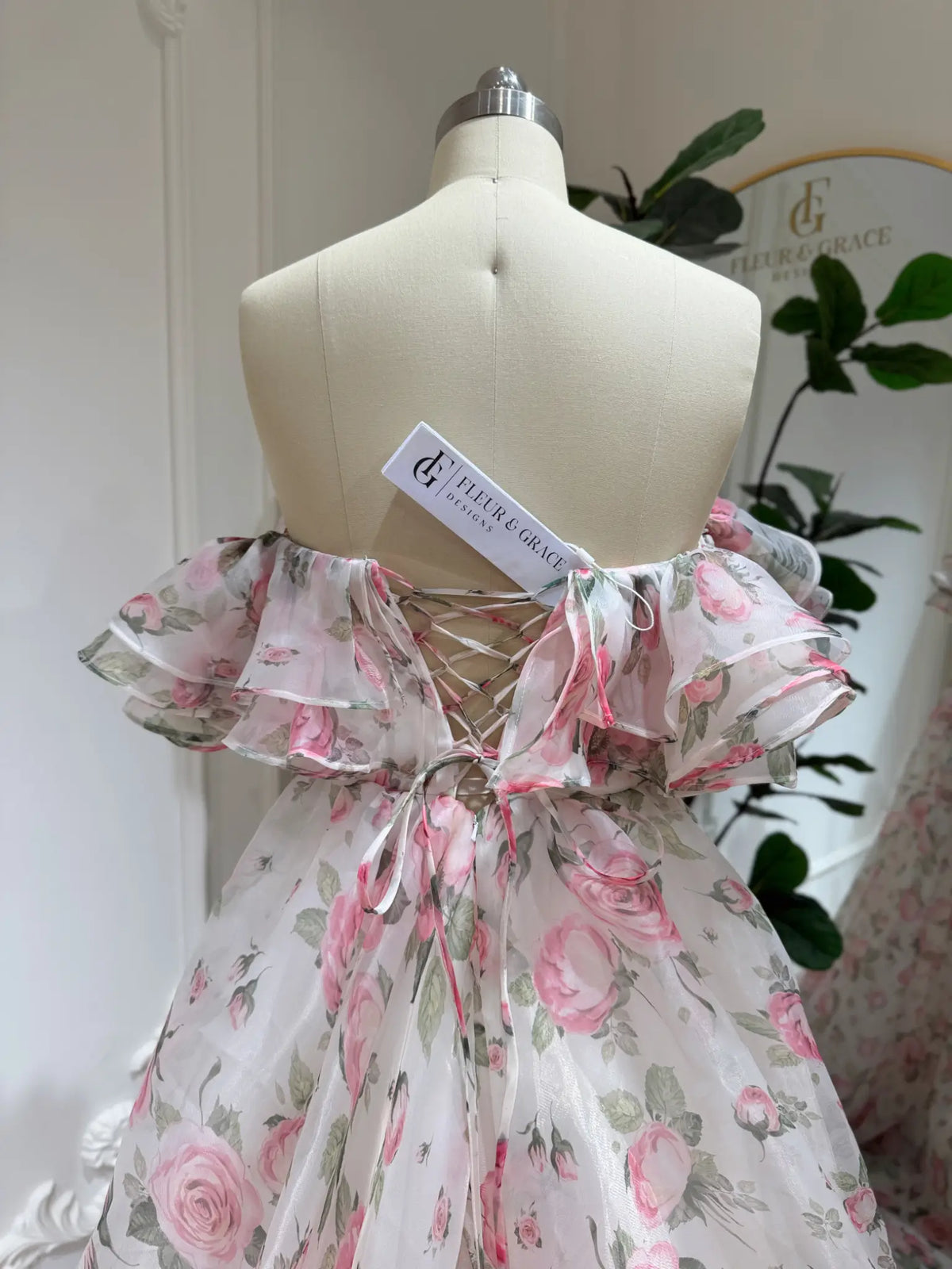 Rosie pink floral organza gown with off-the-shoulder tiered ruffles and a lace-up back on a mannequin.