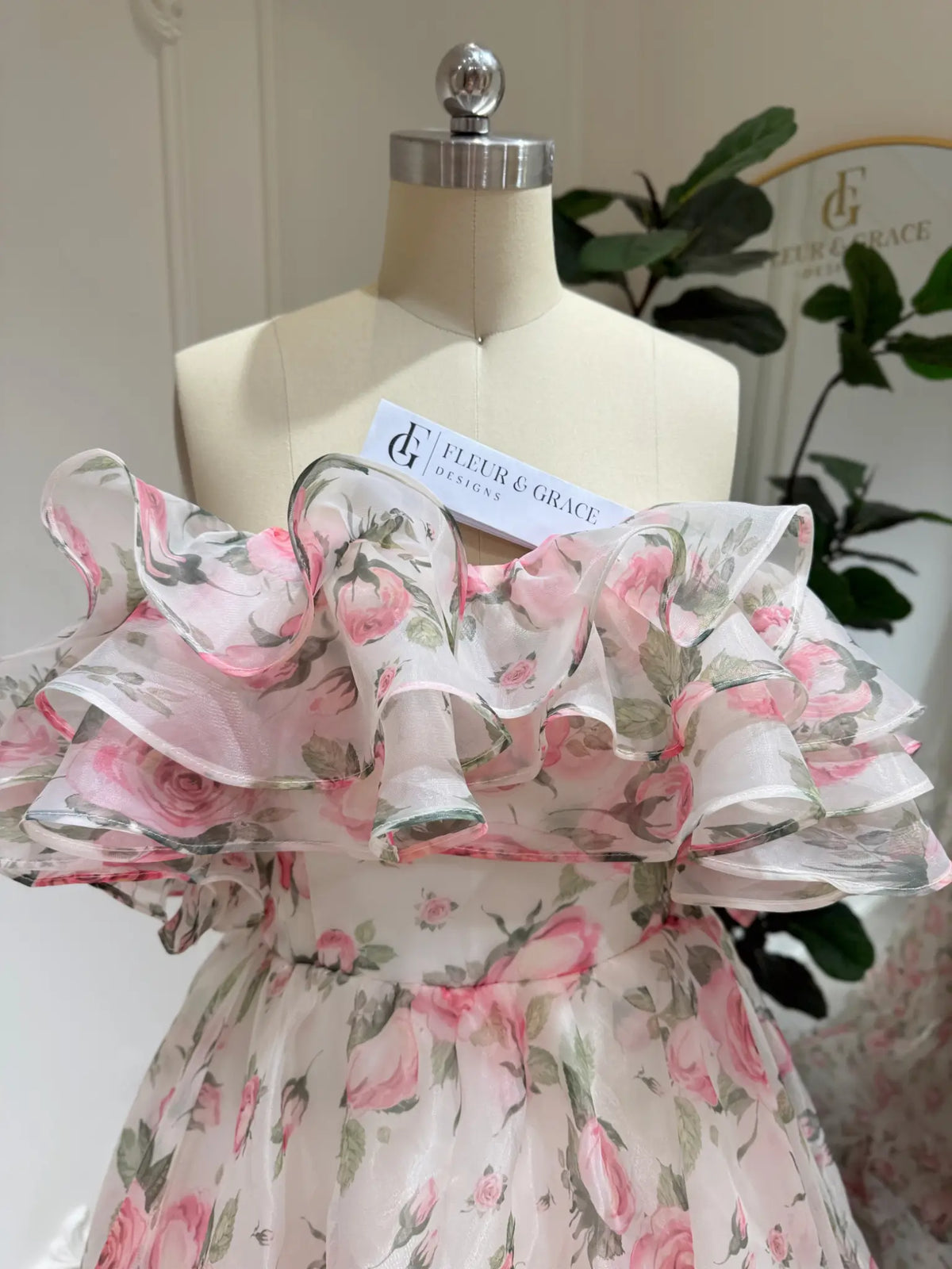 Rosie pink floral organza gown with a tiered ruffle off-the-shoulder neckline on a dress form.