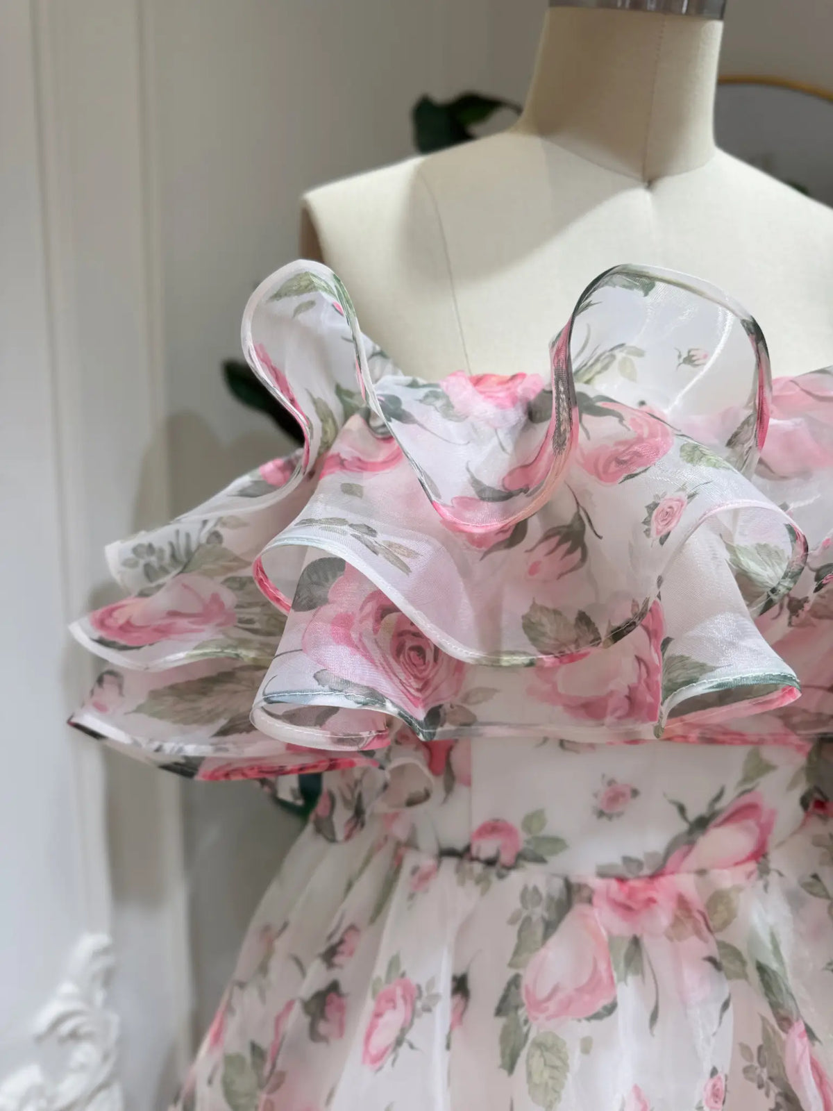 Off-the-shoulder pink floral organza gown with a dramatic tiered ruffle neckline on a dress form.