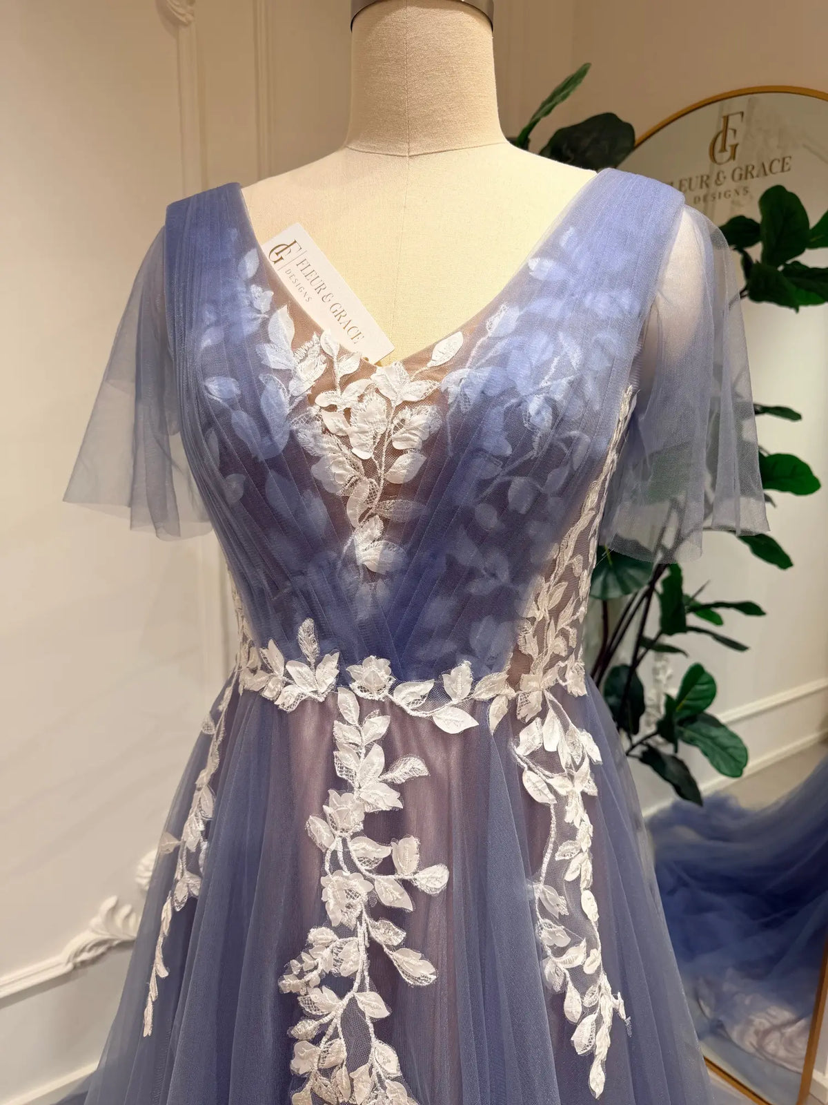 Dusty blue A-line wedding dress featuring a V-neck illusion bodice, delicate white floral lace, and romantic flutter sleeves.