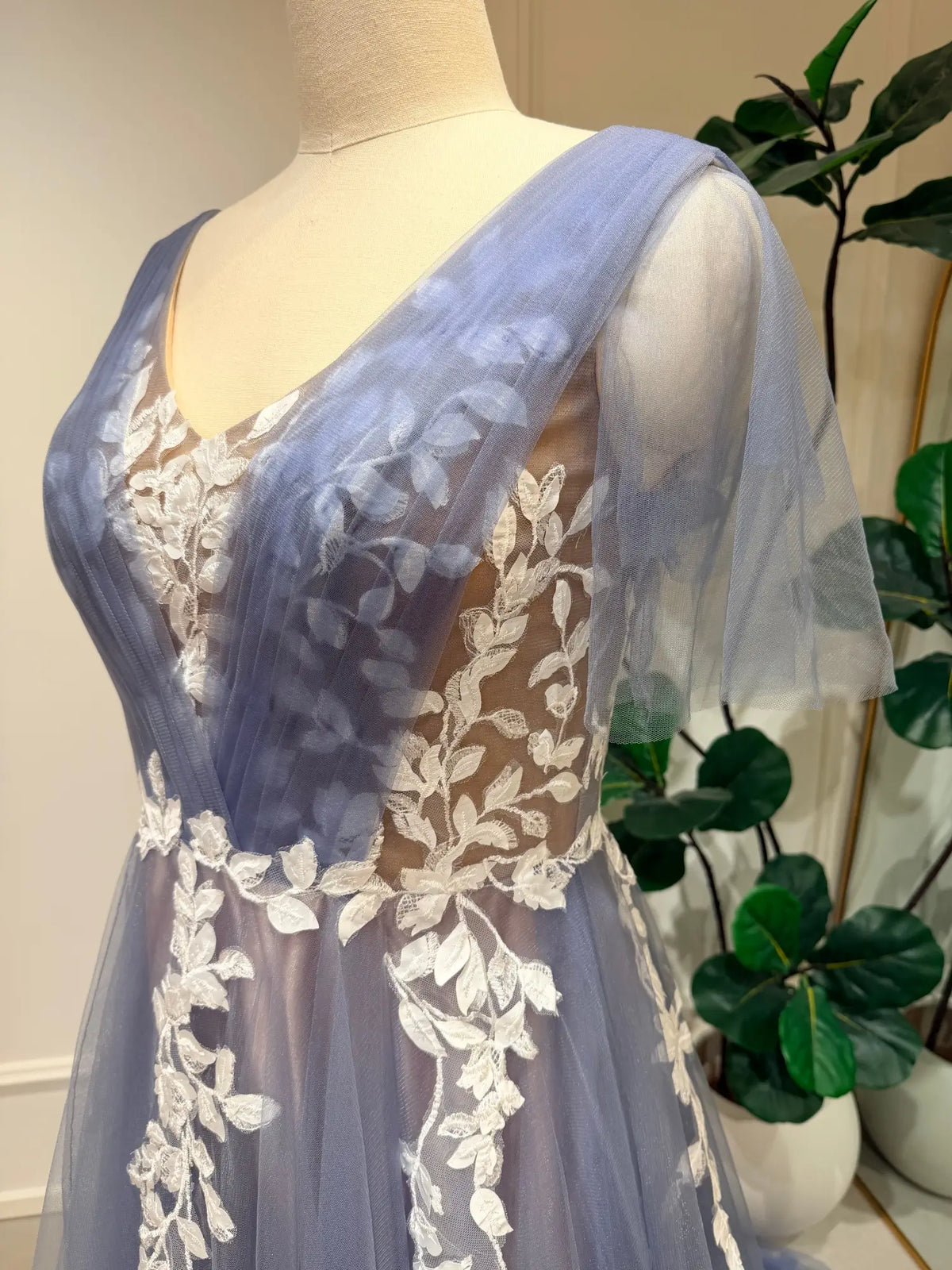 Dusty blue A-line wedding dress featuring a V-neck illusion bodice, delicate white floral lace, and romantic flutter sleeves.