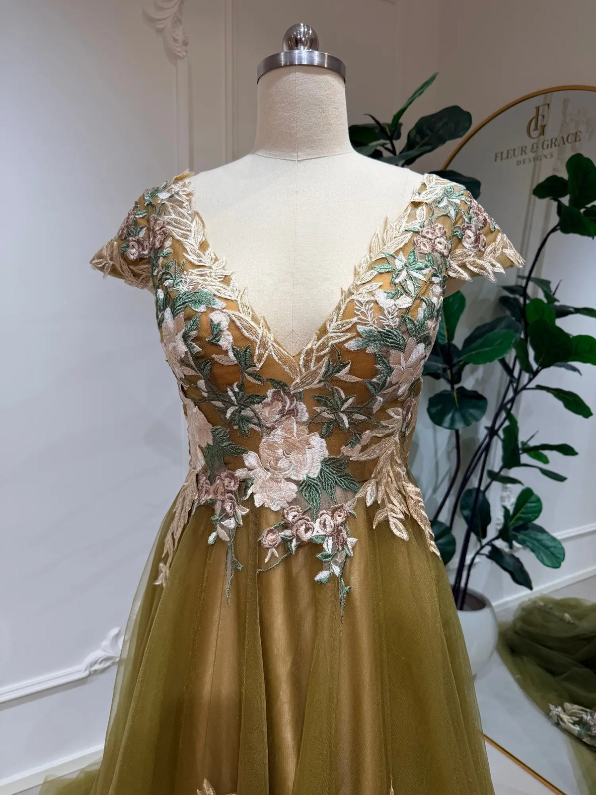 Olive green wedding dress with V-neck bodice, floral embroidery, and flowing tulle skirt on a mannequin.