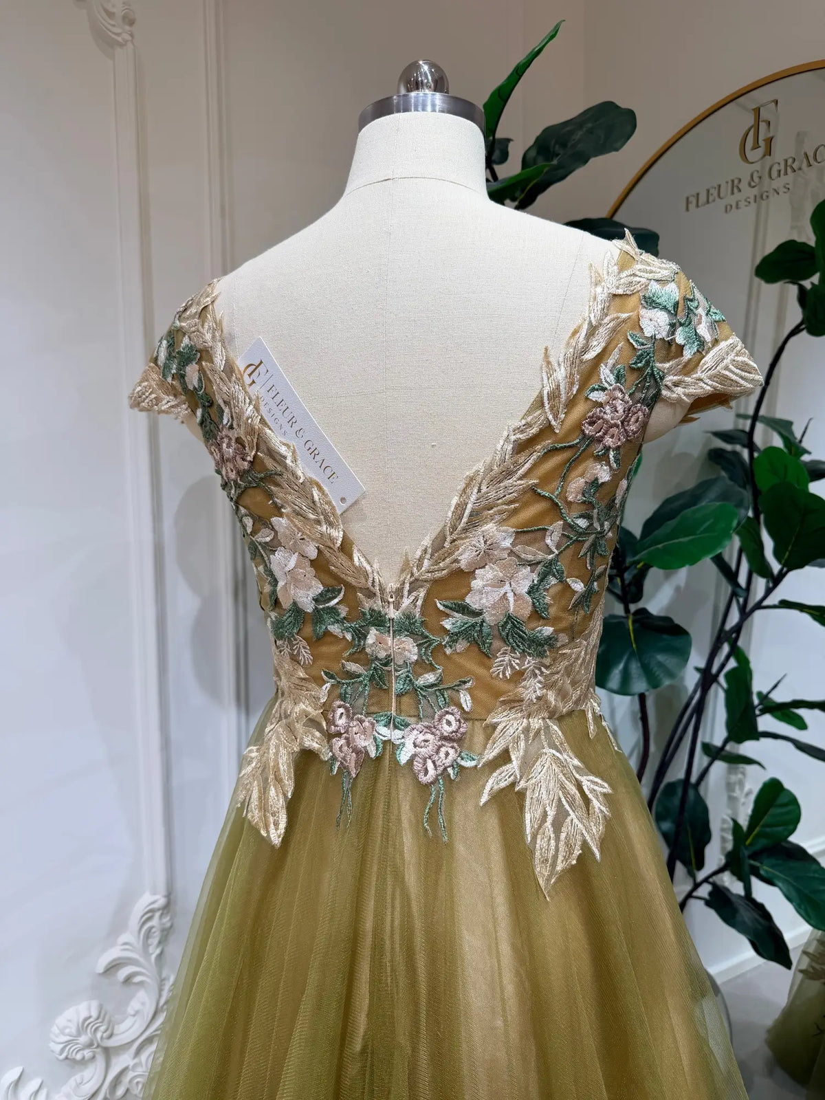 Olive green wedding dress with intricate floral embroidery, V-neck bodice, and flowing tulle skirt on a mannequin.