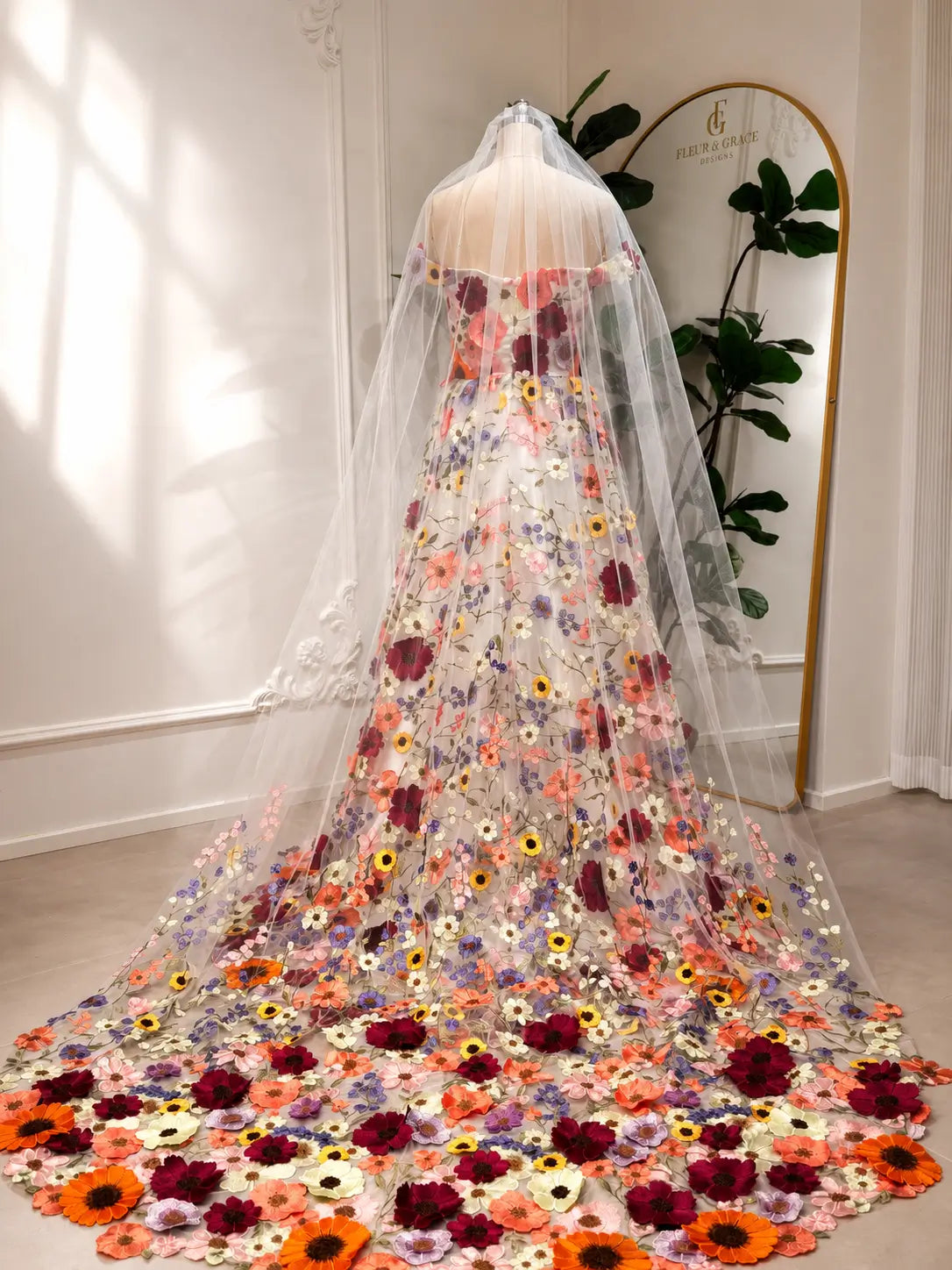 Off-shoulder ivory wedding dress with vibrant wildflower embroidery, tulle skirt, and a long matching floral veil.