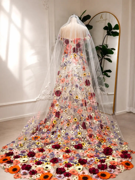 Off-shoulder ivory wedding dress with vibrant wildflower embroidery, tulle skirt, and a long matching floral veil.