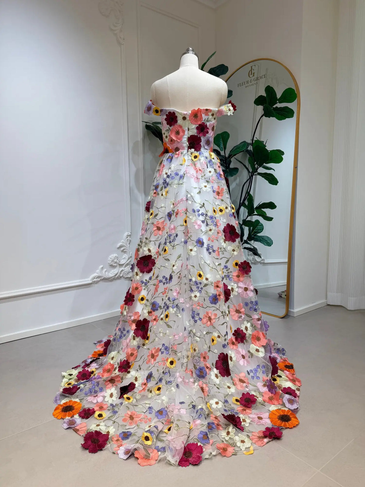 Off-shoulder ivory wedding dress with vibrant, cascading wildflower embroidery and a dramatic floral-trimmed train.