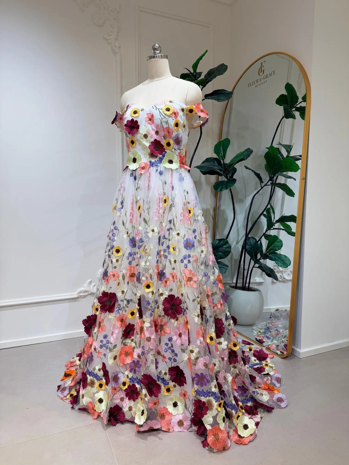 Off-shoulder ivory wedding dress with vibrant, colorful floral embroidery on a flowing A-line tulle skirt.