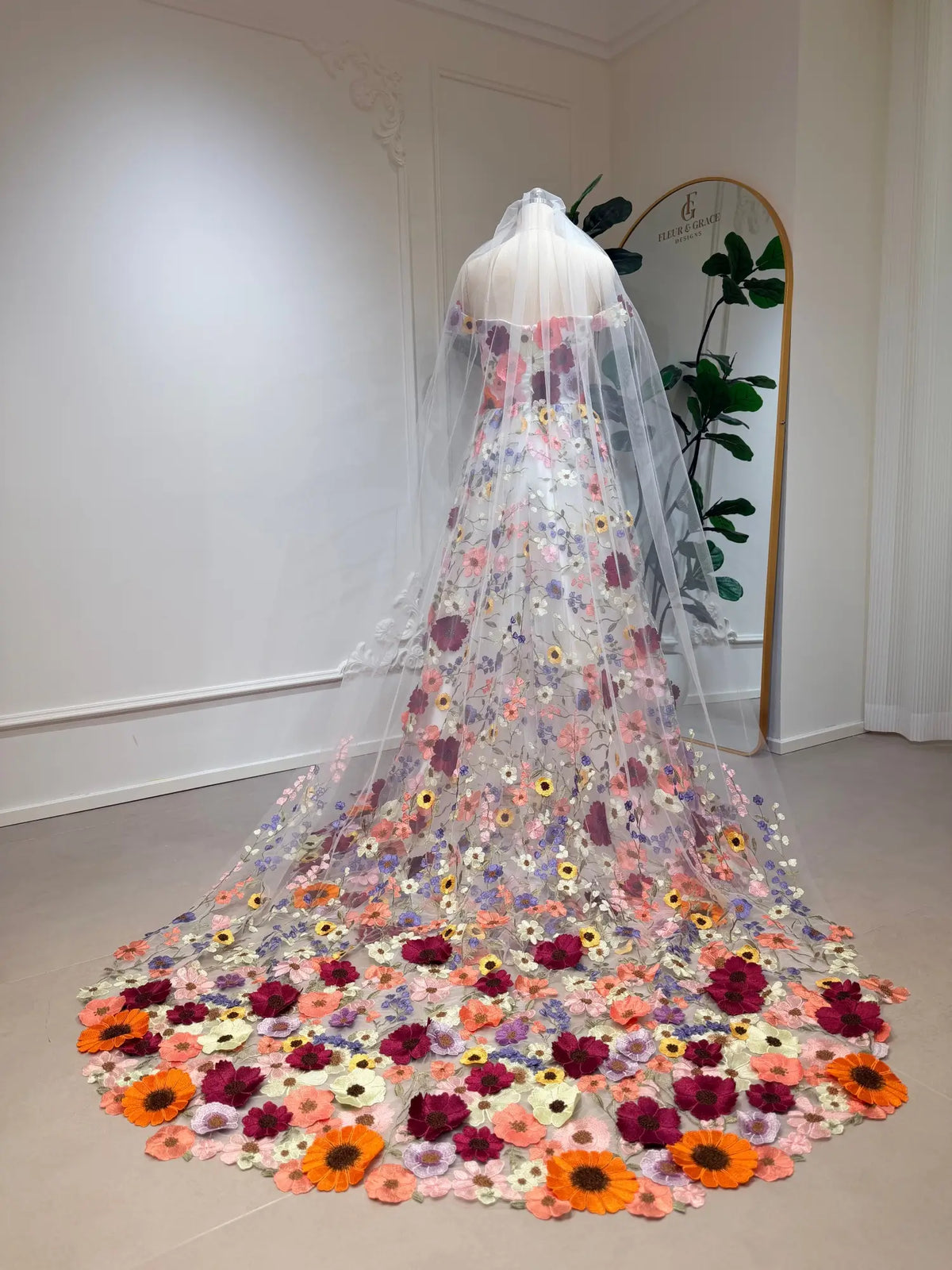Ivory A-line wedding dress with vibrant floral embroidery, off-shoulder sleeves, and a dramatic wildflower-inspired train.
