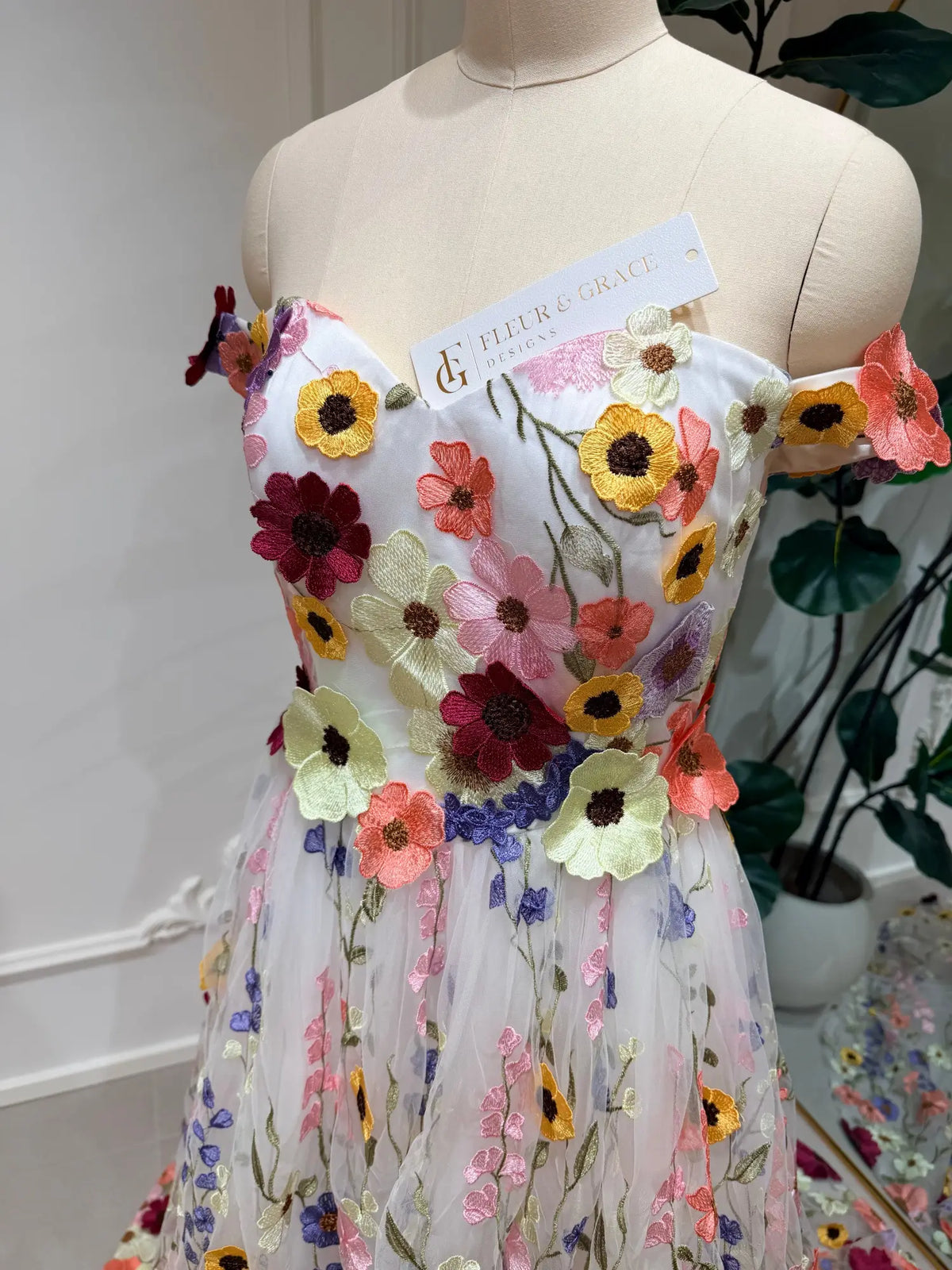 Ivory tulle wedding dress featuring vibrant, colorful floral embroidery and an elegant off-the-shoulder neckline.
