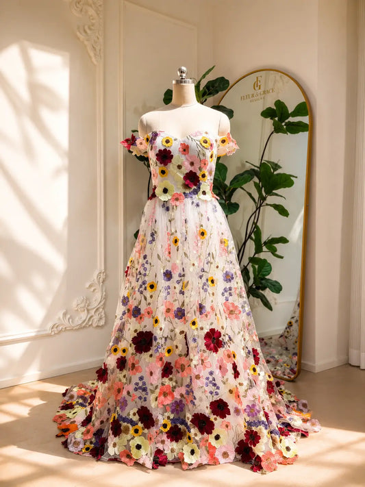 Ivory A-line wedding dress with vibrant floral embroidery, off-shoulder sleeves, and a romantic wildflower tulle skirt.