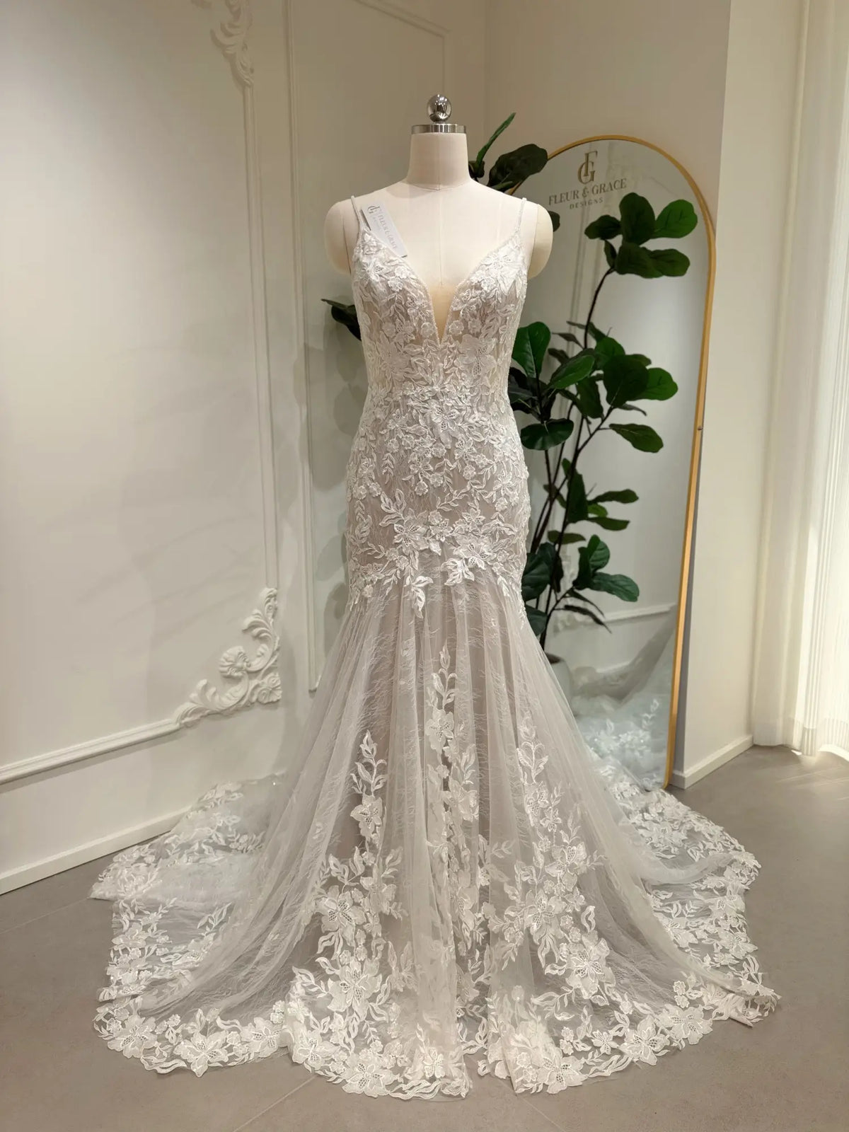Ivory mermaid wedding dress with floral lace appliqués, deep V-neckline, and nude lining on a bridal mannequin.