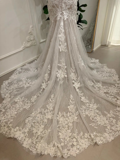 Ivory mermaid wedding dress featuring intricate floral lace appliqués and a dramatic chapel-length tulle train.