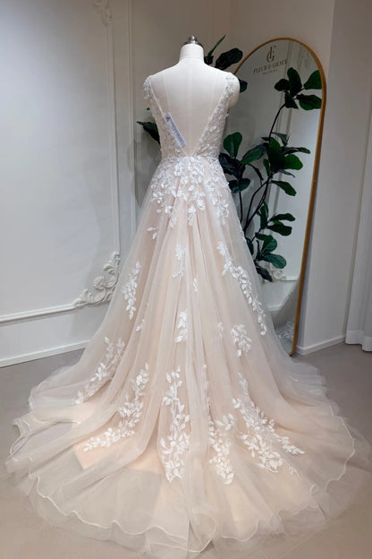 Champagne A-line wedding dress with floral lace appliqué, deep V-back, and flowing tulle skirt on a mannequin.