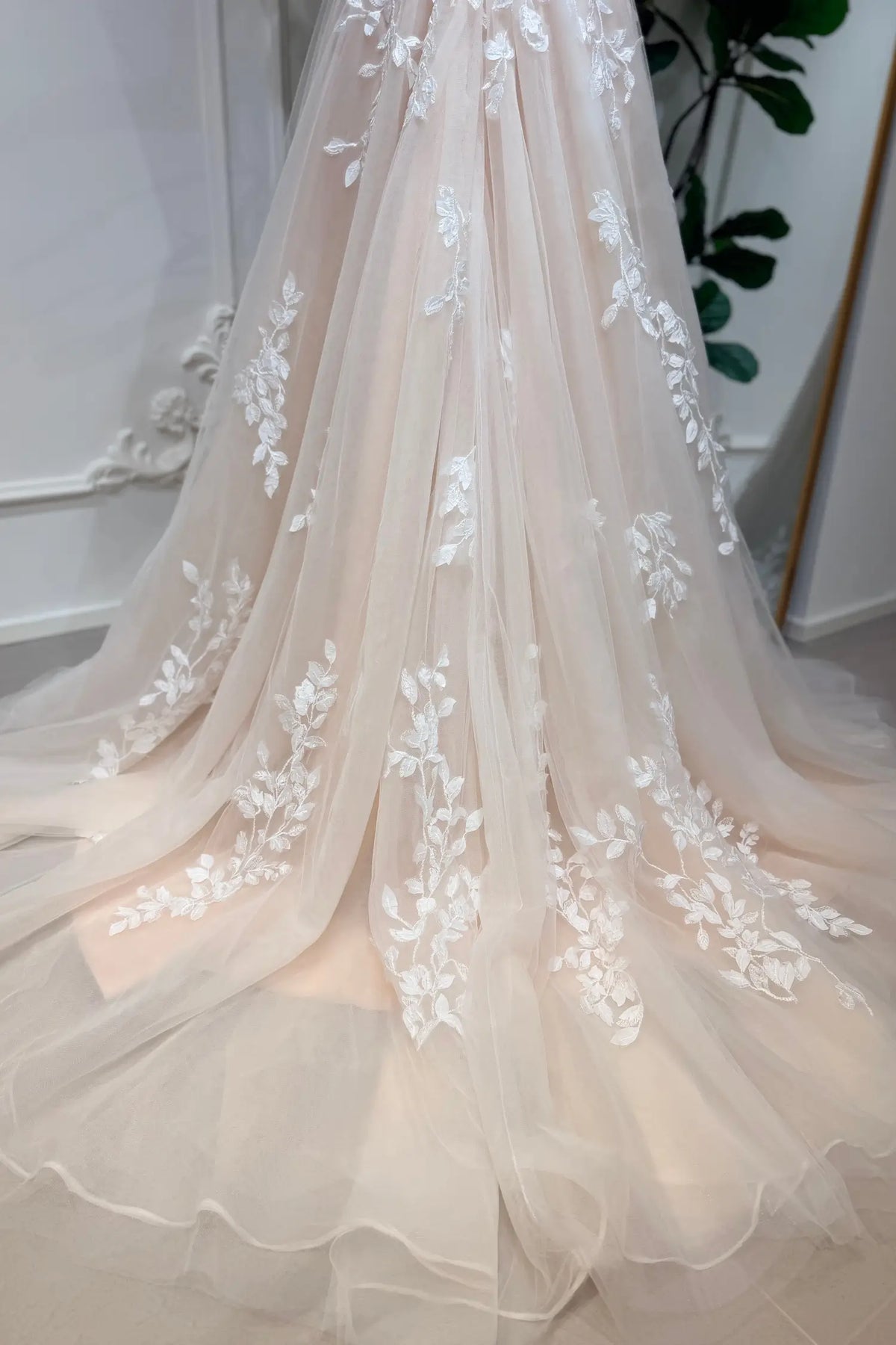 Champagne A-line wedding dress in airy tulle with delicate white floral lace appliqué and a flowing train.