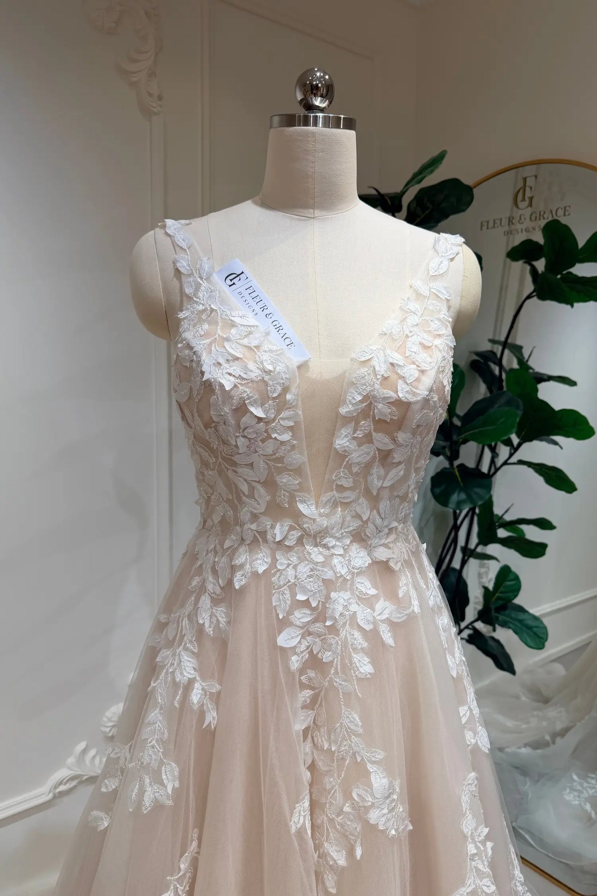 Champagne A-line wedding dress with a deep illusion V-neckline and intricate white floral lace appliqué on tulle.