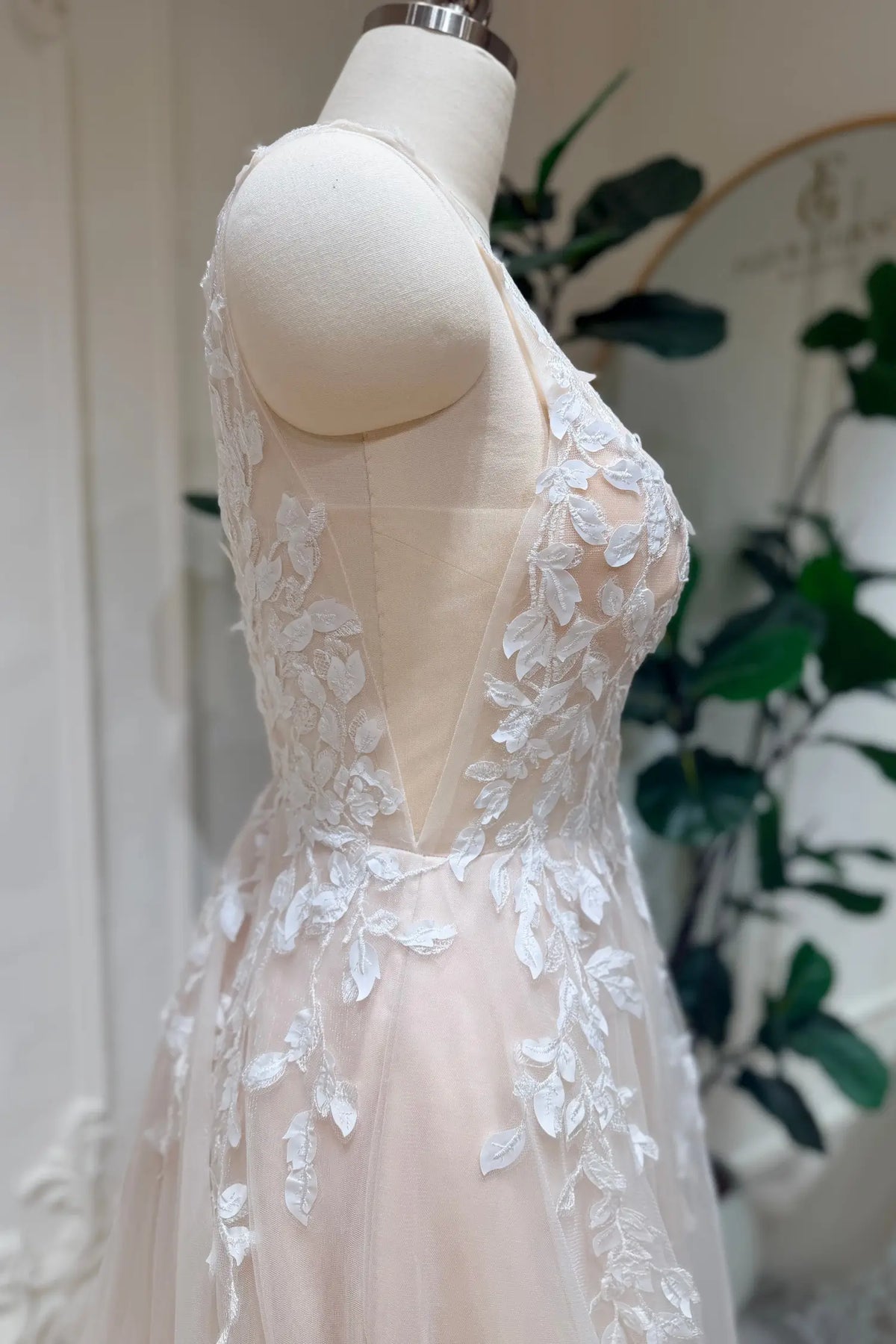 Champagne A-line wedding dress with floral lace appliqué, illusion side panels, and airy tulle on a dress form.