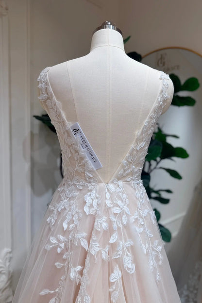 Champagne A-line wedding dress with a deep V-back, delicate floral lace appliqué, and soft tulle layers on a mannequin.