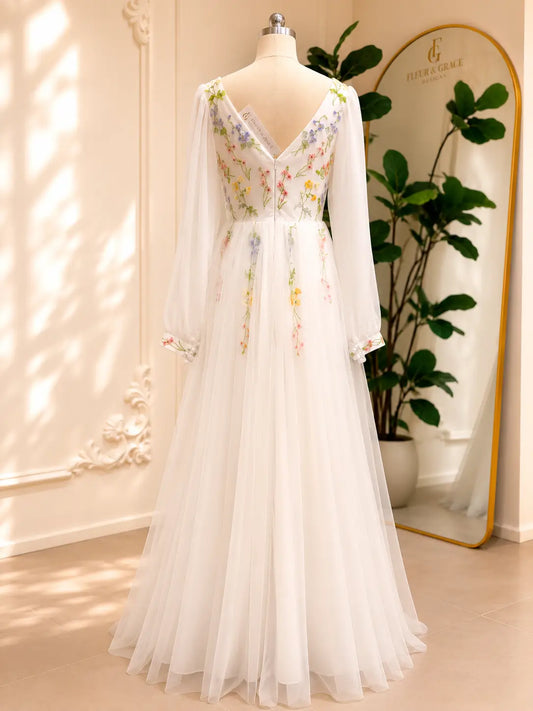 Back view of a white A-line wedding dress with pastel floral embroidery, sheer bishop sleeves, and a flowing tulle skirt.