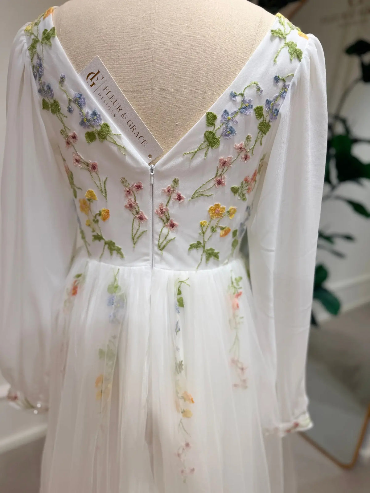 White A-line wedding dress featuring pastel floral embroidery, sheer bishop sleeves, and a romantic V-back design.