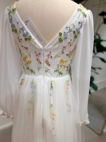 White A-line wedding dress featuring pastel floral embroidery, sheer bishop sleeves, and a romantic V-back design.