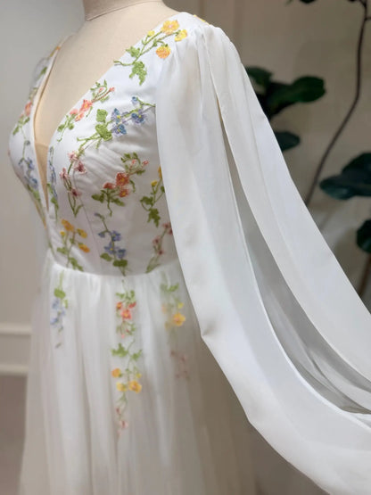 A-line wedding dress with pastel floral embroidery, deep V-neck, and airy chiffon bishop sleeves on a tulle skirt.