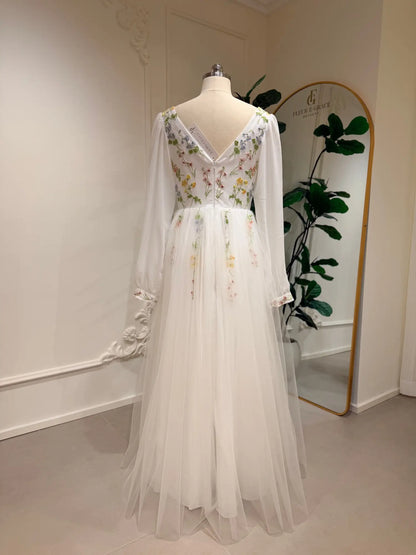 Back view of a white A-line wedding dress with pastel floral embroidery, sheer bishop sleeves, and a flowing tulle skirt.
