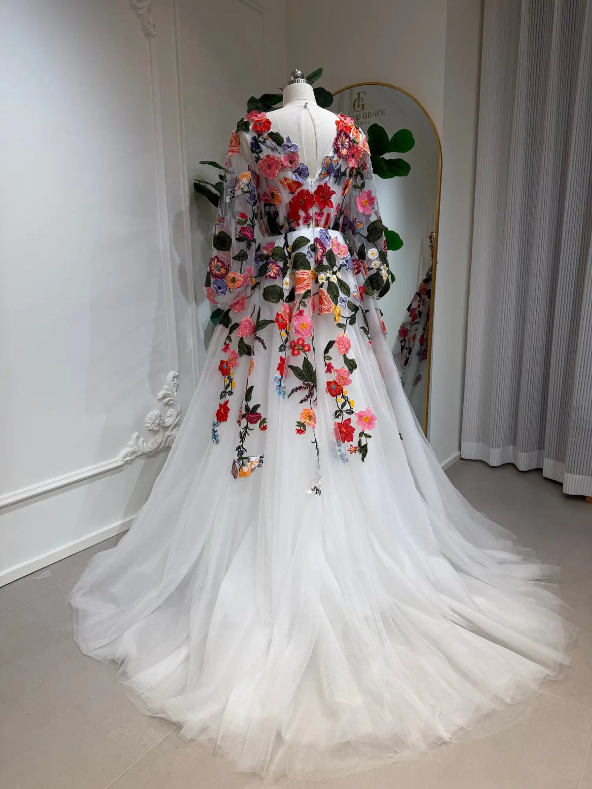 Back view of a white tulle wedding dress with vibrant floral embroidery, long bishop sleeves, and an illusion V-back.