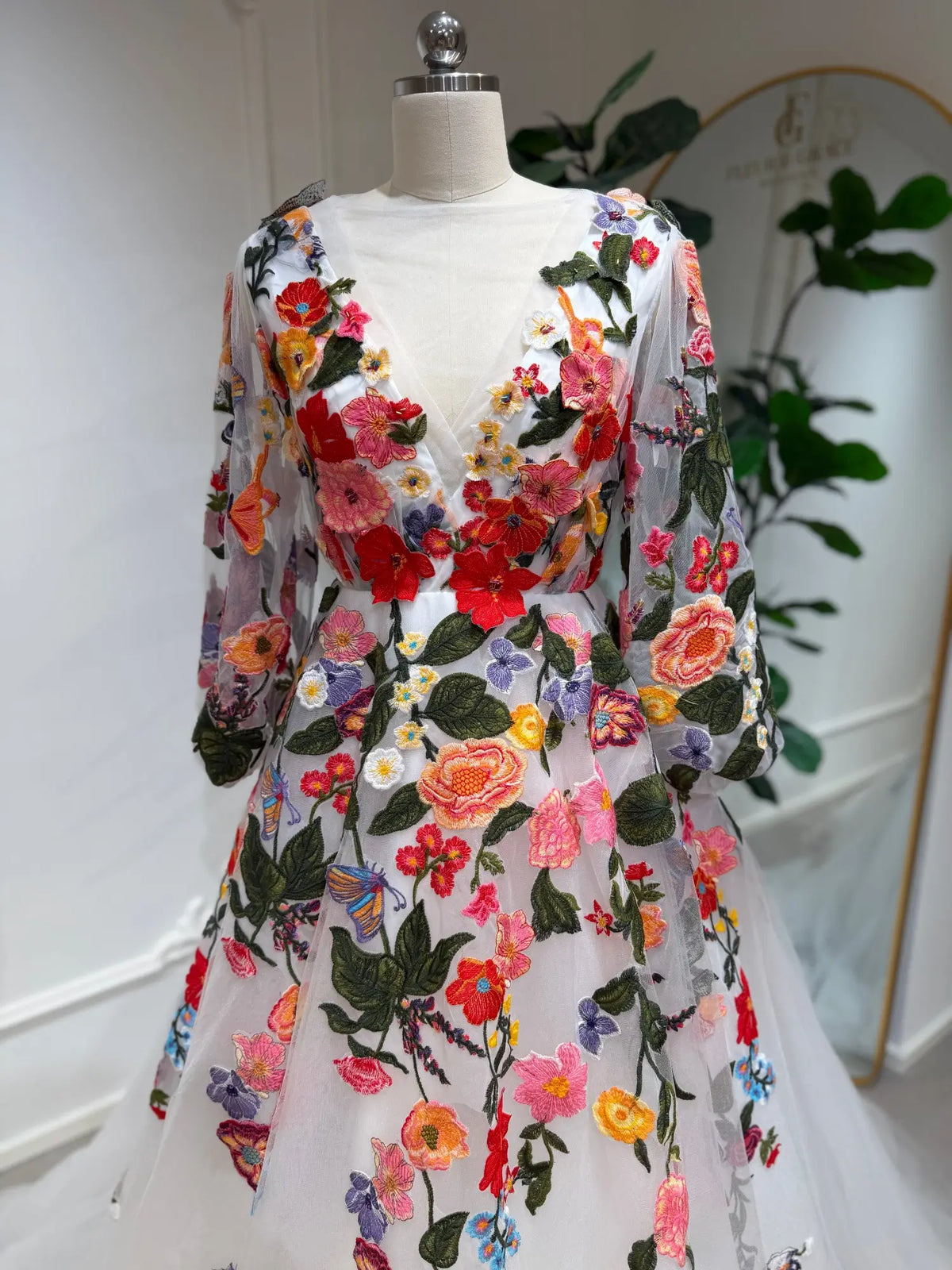 Suri wedding dress with vibrant floral embroidery, illusion V-neck, and sheer long bishop sleeves on tulle.