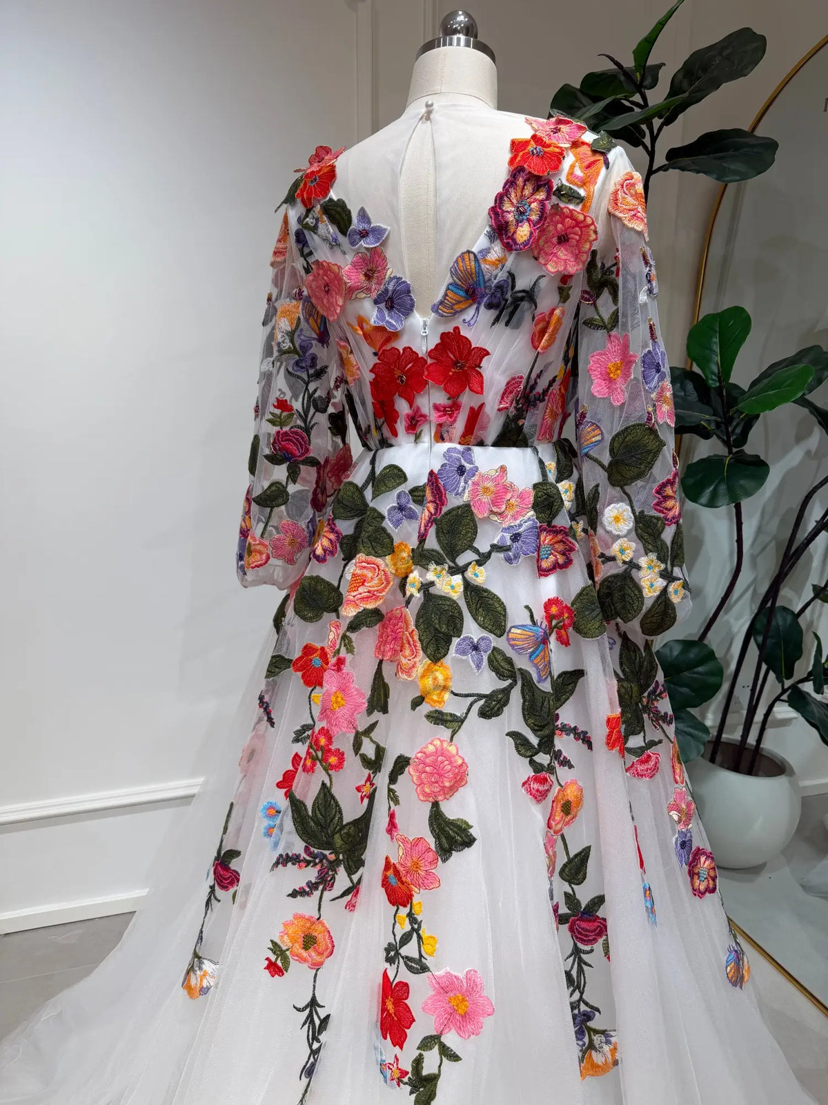 Suri wedding dress featuring vibrant 3D floral embroidery, sheer long sleeves, and a flowing tulle A-line skirt.