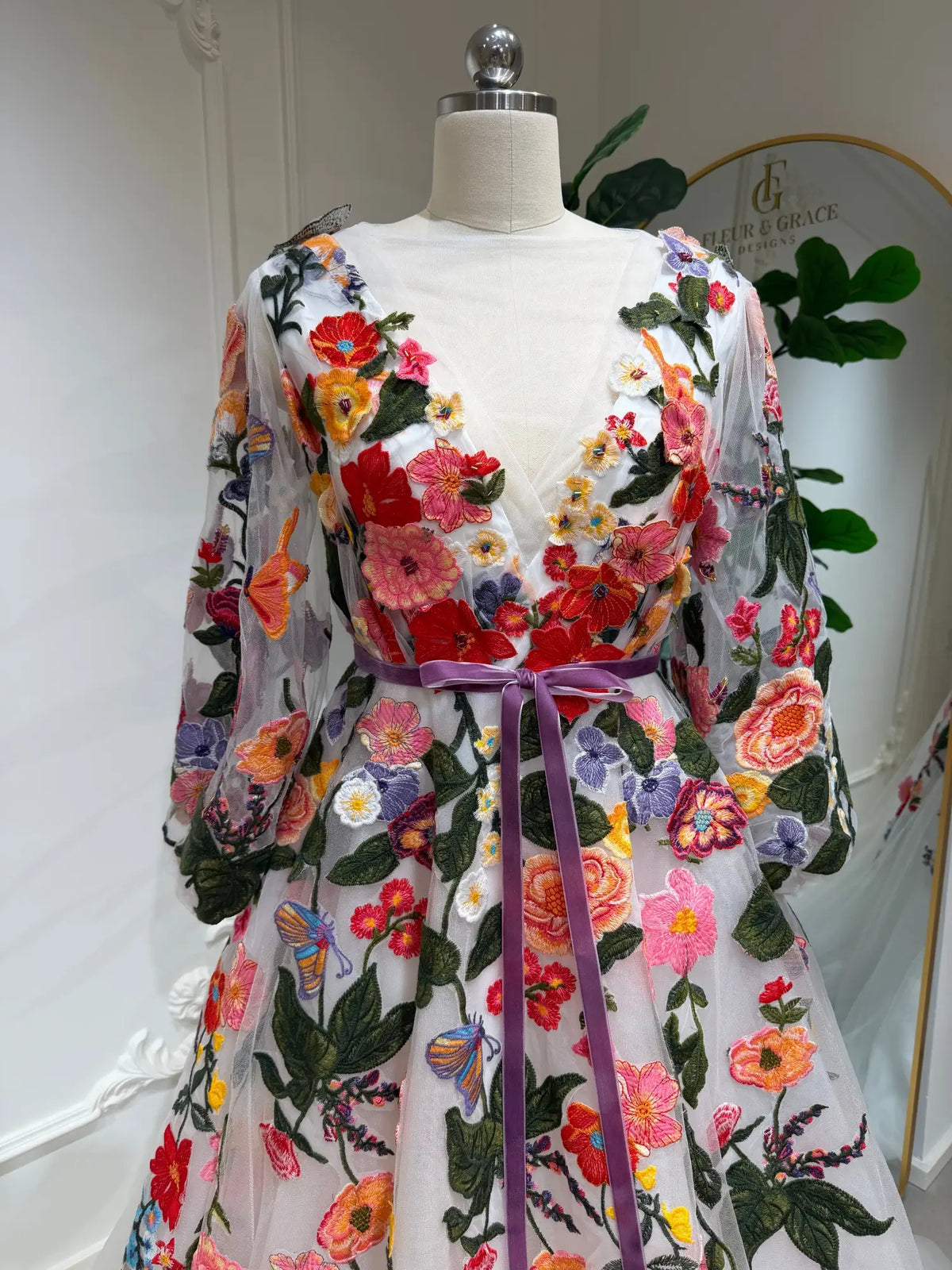Suri wedding dress with vibrant floral embroidery, sheer long sleeves, illusion V-neck, and a purple velvet waist ribbon.