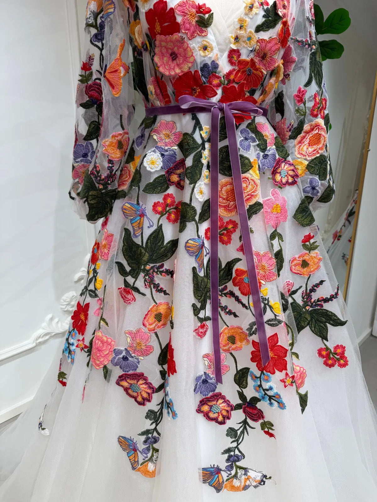 Suri wedding dress with vibrant floral embroidery, sheer long sleeves, and a velvet ribbon belt on white tulle.