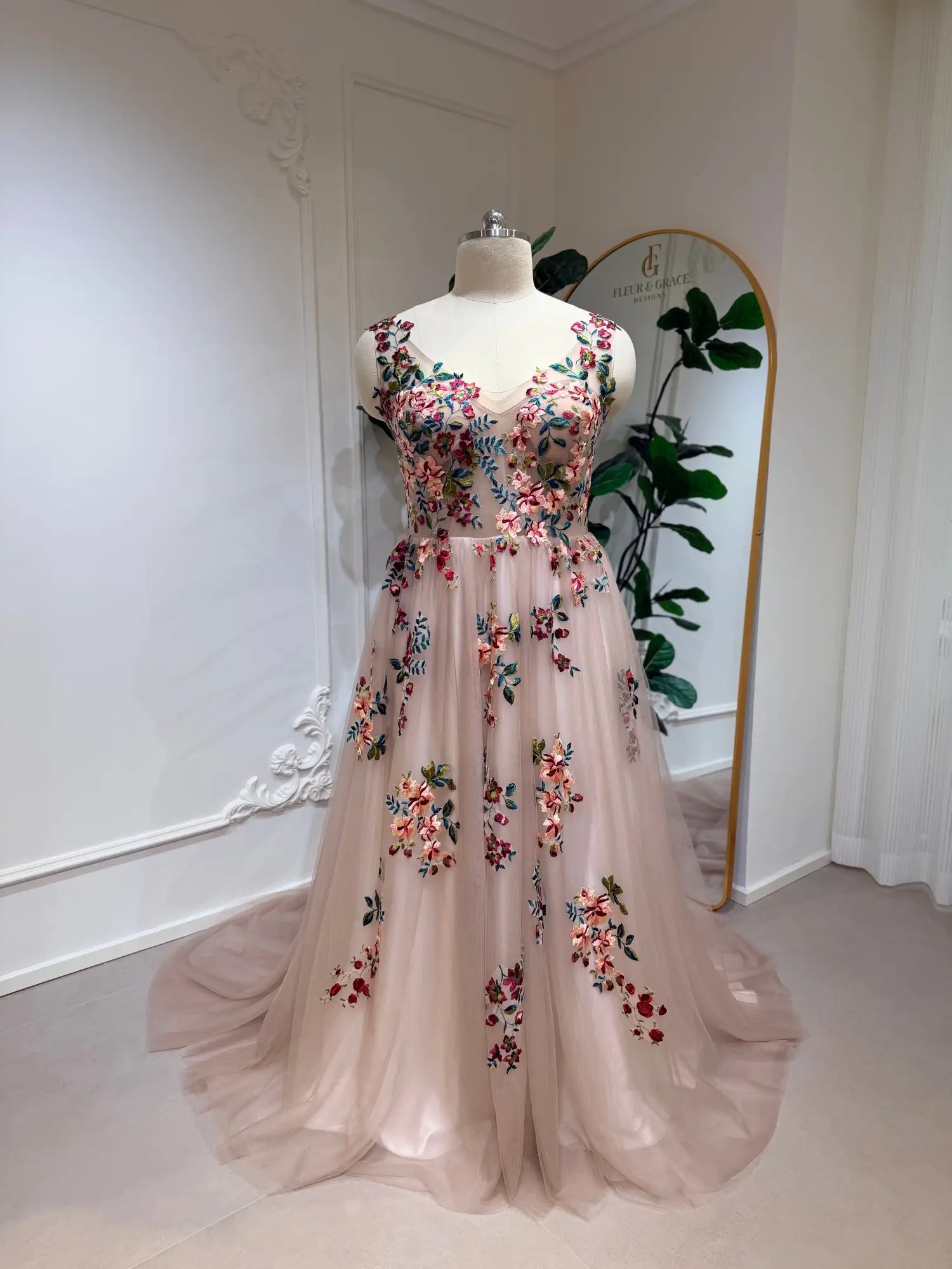 Blush A-line wedding dress featuring an illusion bodice, colorful floral embroidery, and a flowing tulle chapel train.