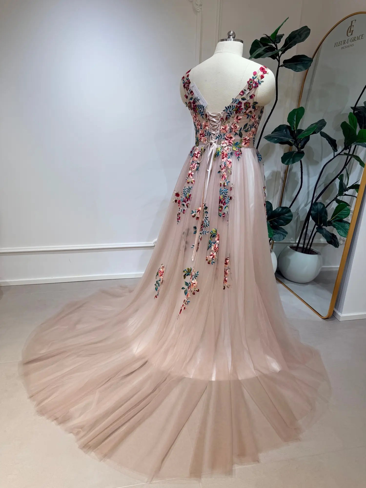 Blush tulle wedding dress with colorful floral embroidery, illusion V-back, and adjustable corset lace-up closure.