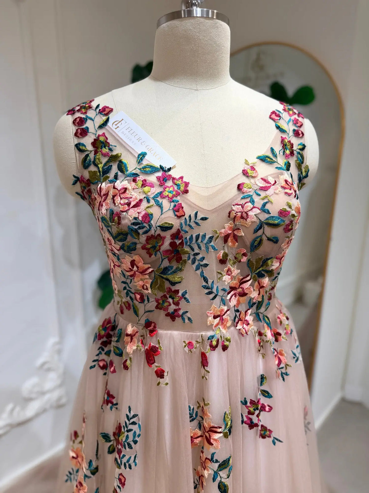 Blush tulle wedding dress featuring an illusion bodice with vibrant multicolored floral embroidery and a sweetheart neckline.