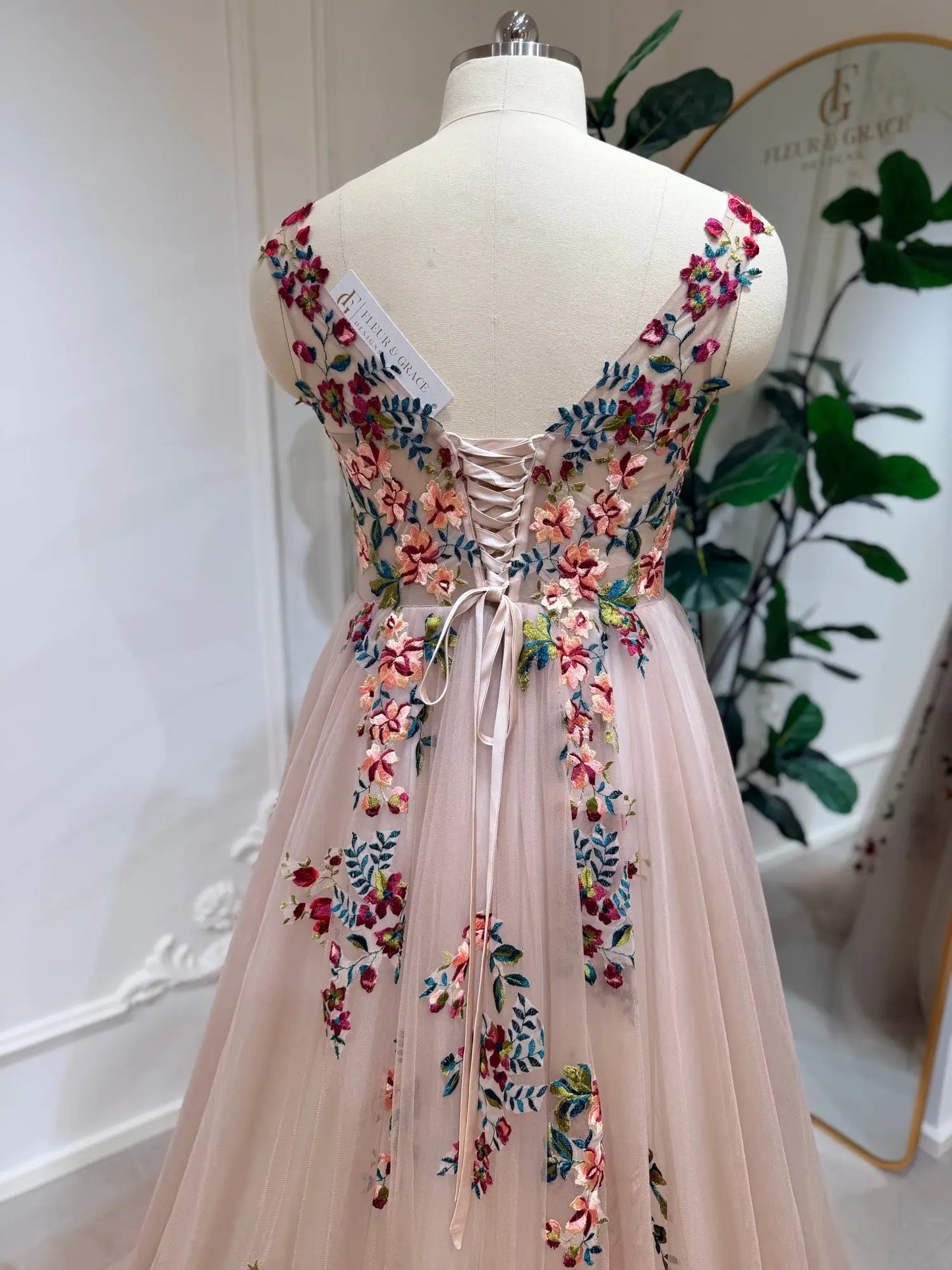 Blush A-line wedding dress with colorful floral embroidery, illusion V-back, and adjustable corset lace-up closure.
