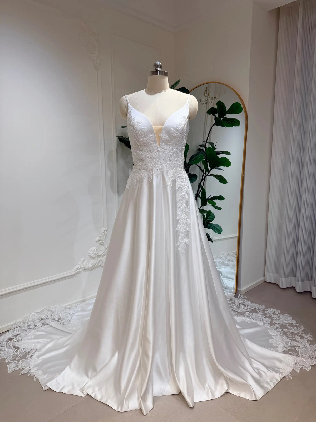 White satin A-line wedding dress with a deep V-neck, floral lace bodice appliqué, and a long lace-trimmed train.