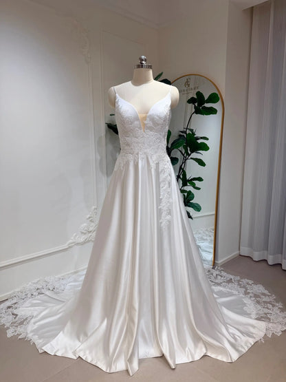 White satin A-line wedding dress with a deep V-neck, floral lace bodice appliqué, and a long lace-trimmed train.