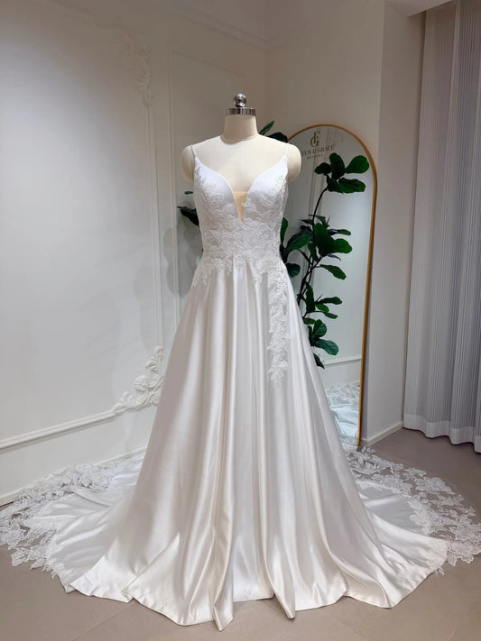 White satin A-line wedding dress with a deep V-neck, floral lace bodice appliqué, and a long lace-trimmed train.