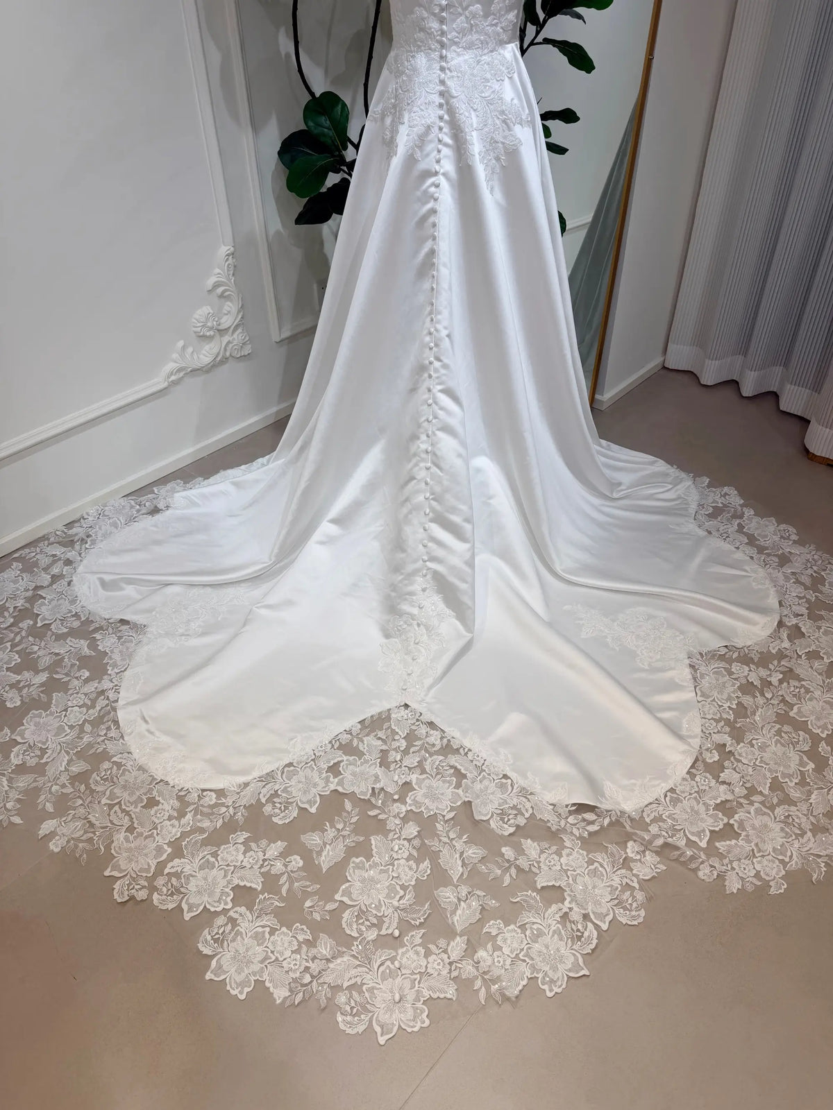 White satin A-line wedding dress with a button-back bodice and an intricate floral lace appliquéd train.
