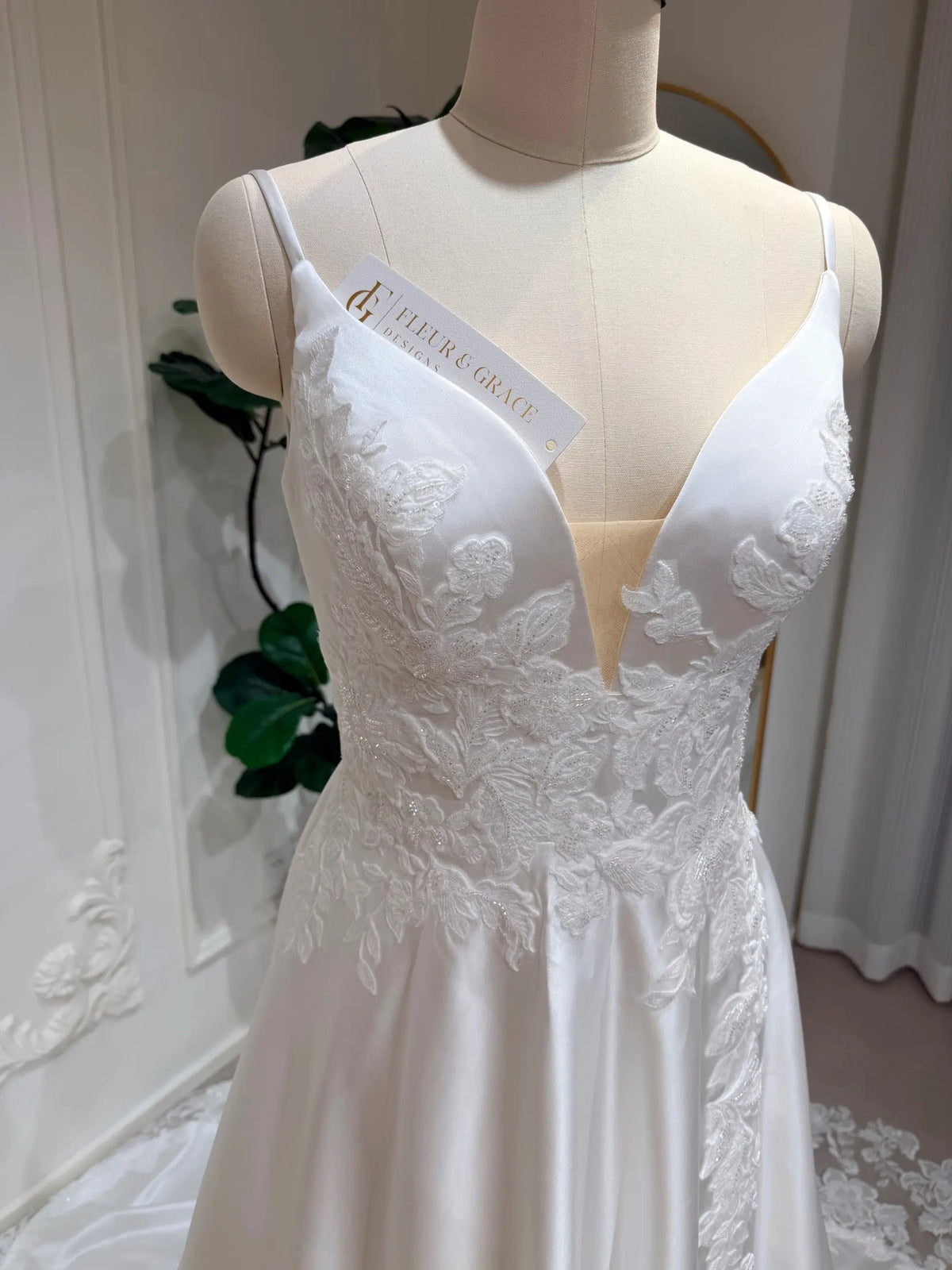 White satin A-line wedding dress with a deep V-neck, illusion bodice, and delicate floral lace appliqué.