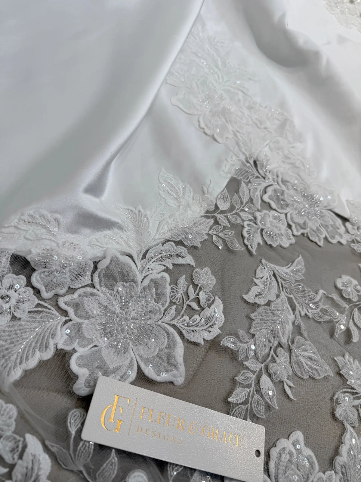 White satin wedding dress fabric featuring intricate floral lace appliqué with delicate sequin detailing.